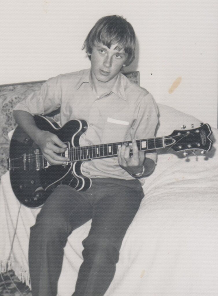 Black and white photo of a teenage boy playing a hollow-body Aria electric guitar
